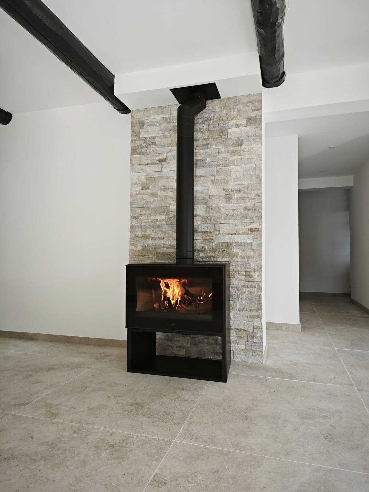 Poêle à bois DENIA FINLAND installé à Bédarrides (84370) par Flamme Concept, le poêle est très modèrne avec un fond en parrement de pierre moderne, le poêle est allumé avec une grande flamme.