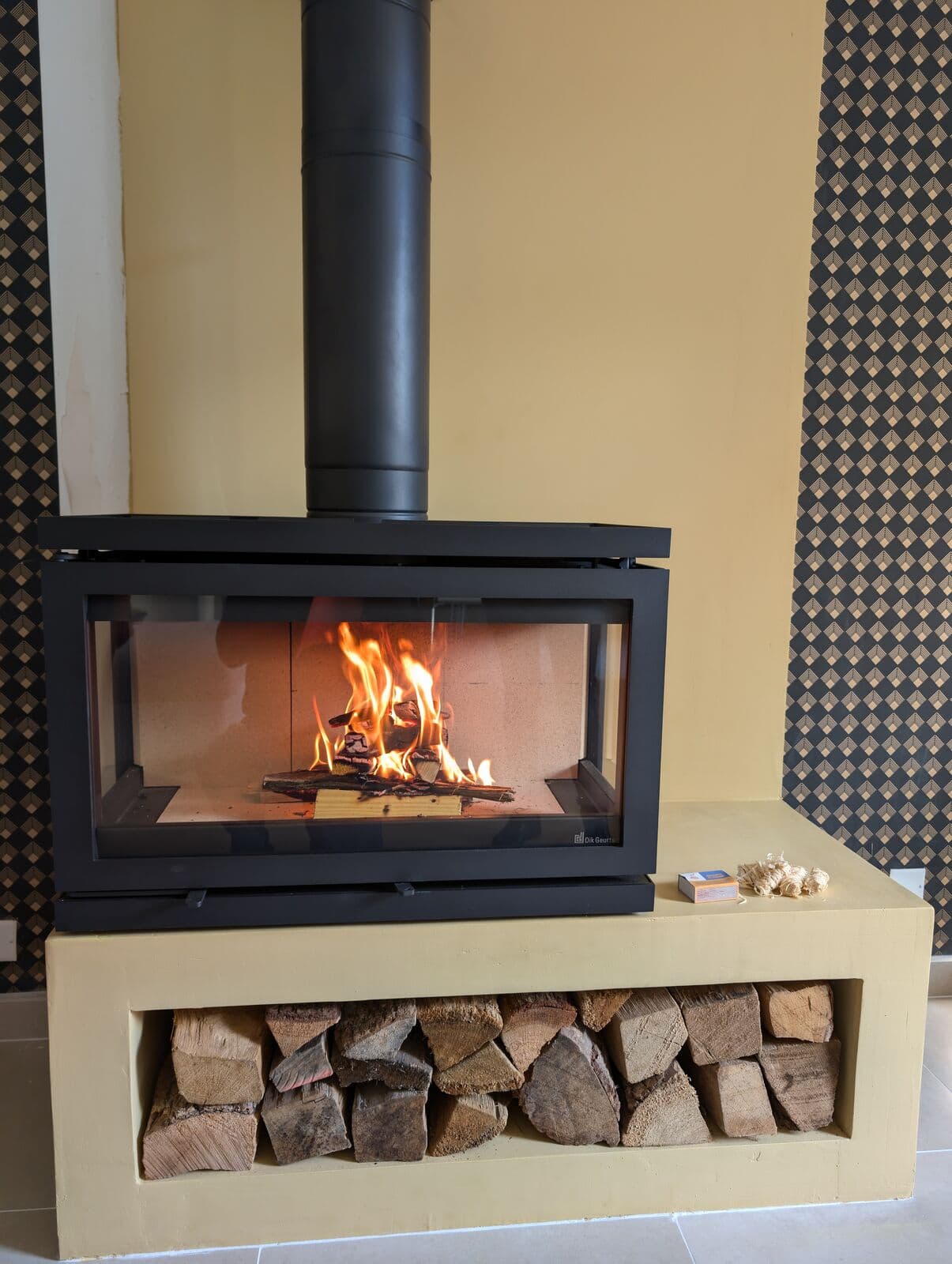 Poêle à bois Vidar Triple à Avignon avec vitre trois faces, installé sur un socle maçonné avec réserve à bois, par Flamme Concept